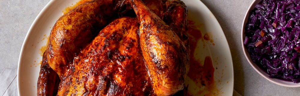Auf dem Bild ist eine ganze, gegarte Pute zu sehen. Die Haut der Pute hat eine schön bräunliche Farbe. Als Beilagen gibt es Rotkohl und Kartoffelknödel. Pute