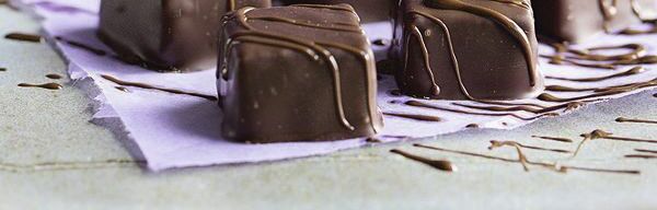 Würfel-Pralinen werden mit Schokolade aus Spritzbeutel verziert - Blätterkrokant-Pralinen Rezept Blätterkrokant-Pralinen