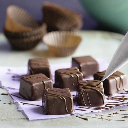 Würfel-Pralinen werden mit Schokolade aus Spritzbeutel verziert - Blätterkrokant-Pralinen Rezept Blätterkrokant-Pralinen