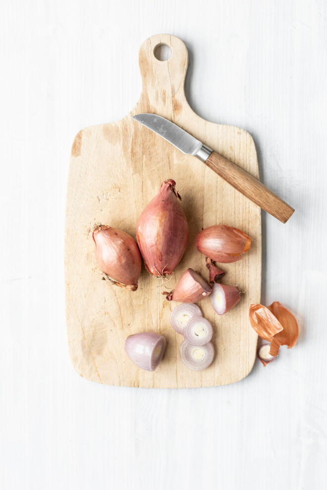 Auf dem Bild sieht man mehrere Schalotten. Einige sind aufgeschnitten. Schalotten